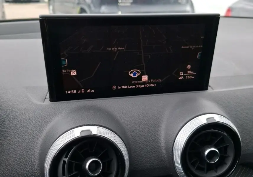 Écran GPS central et aérateurs ronds argentés du tableau de bord d’un Audi Q2 2023 noir, vue intérieure frontale.