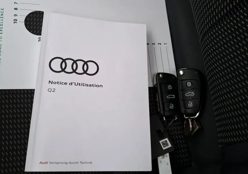 Manuel d'utilisation Audi Q2 posé sur siège tissu noir avec deux clés de voiture noires à côté.