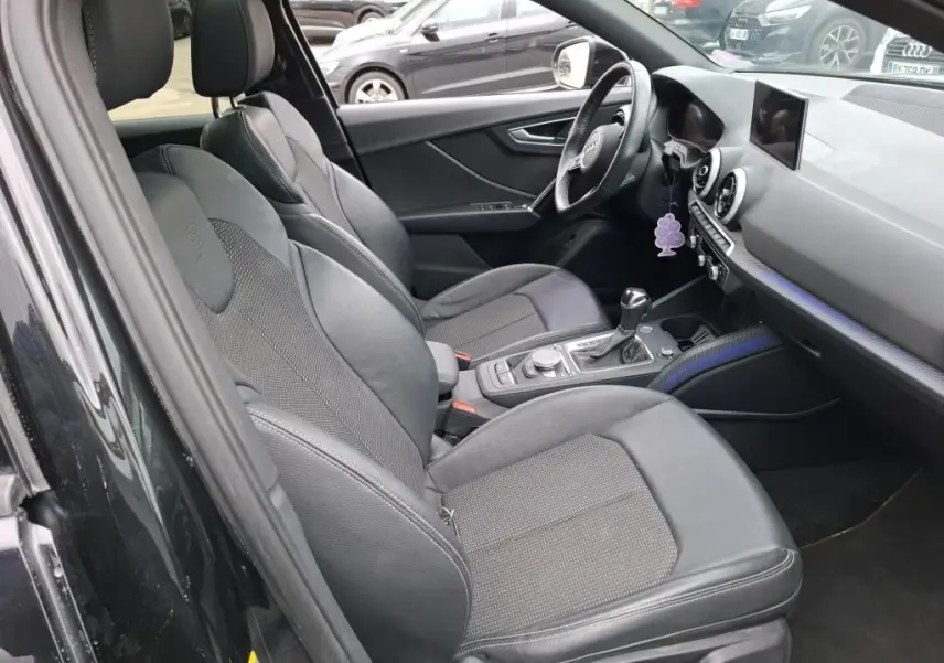 Vue intérieure côté conducteur de l'Audi Q2 noire 2023, sièges sport noirs et tableau de bord avec écran central.