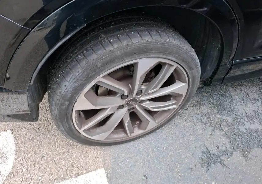 Gros plan sur la roue avant droite avec jante alu grise de l'Audi Q2 noire, version S-Line + 2023.