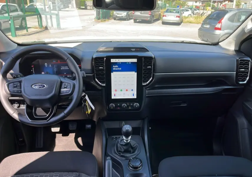 Vue intérieure avant du Ford Ranger 2026, tableau de bord noir avec écran tactile vertical et volant multifonctions.
