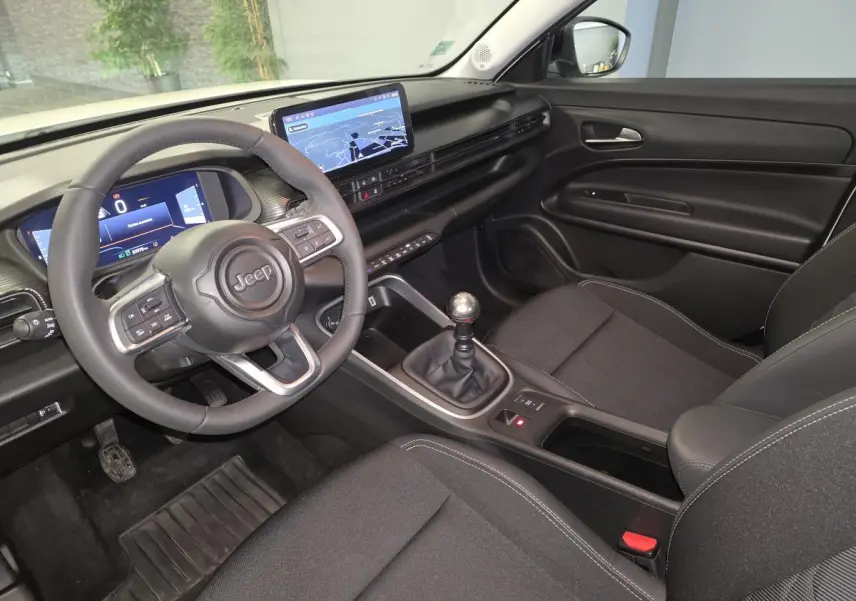 Vue intérieure côté conducteur du Jeep Avenger 2025, volant multifonction, tableau de bord numérique et levier de vitesses manuel.