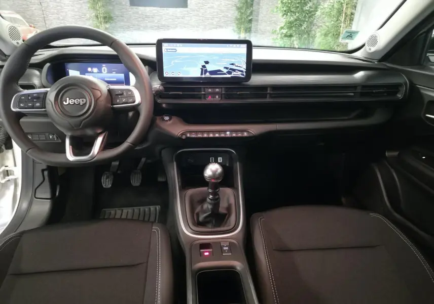 Vue intérieure avant du Jeep Avenger blanc 2025, volant multifonction, écran tactile central et levier de vitesses manuel.