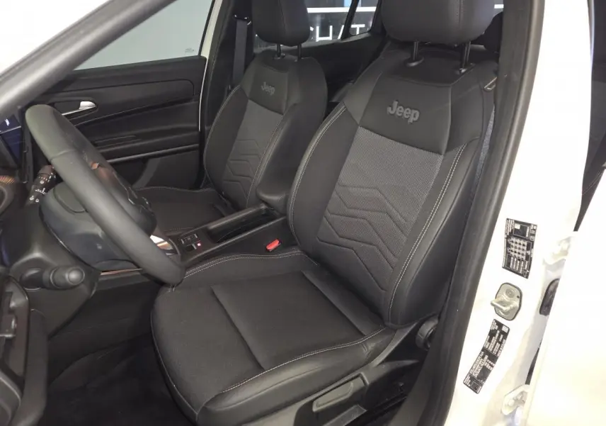 Vue intérieure côté conducteur du Jeep Avenger blanc 2025, sièges noirs mixte tissu/TEP avec logo Jeep brodé.