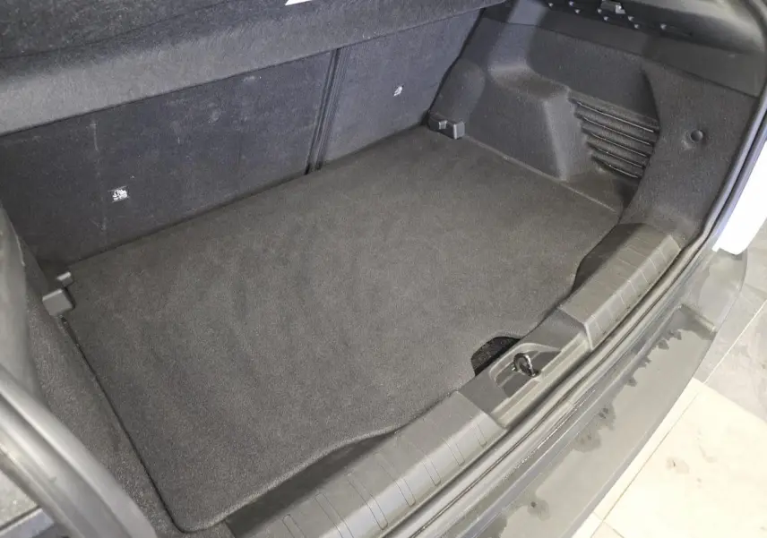 Vue rapprochée du coffre ouvert d'un Jeep Avenger blanc, montrant le tapis de sol noir et les finitions intérieures.