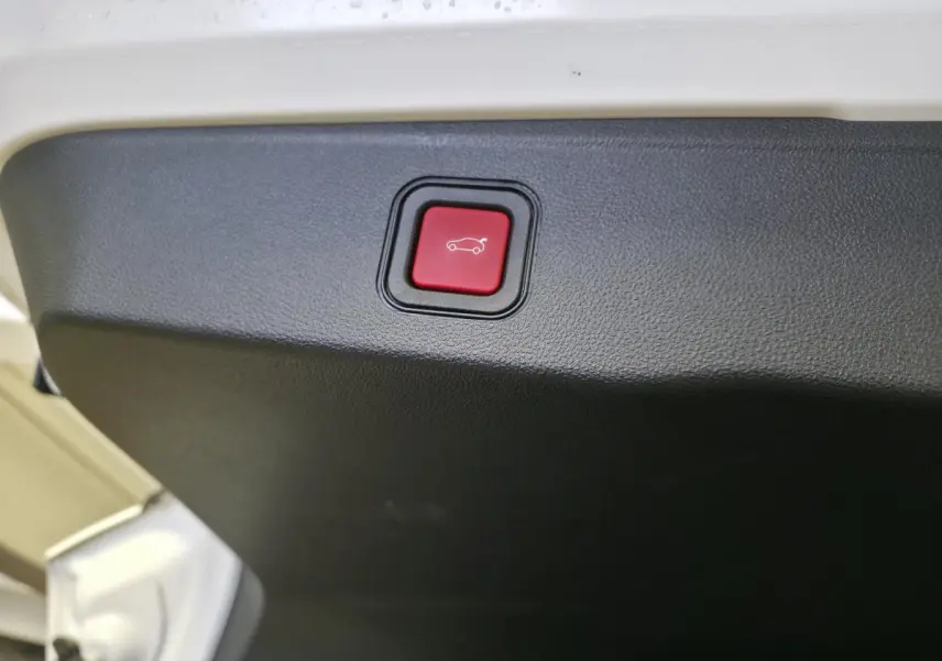 Gros plan sur le bouton rouge d'ouverture électrique mains libres du hayon d'un Jeep Avenger blanc 2025.