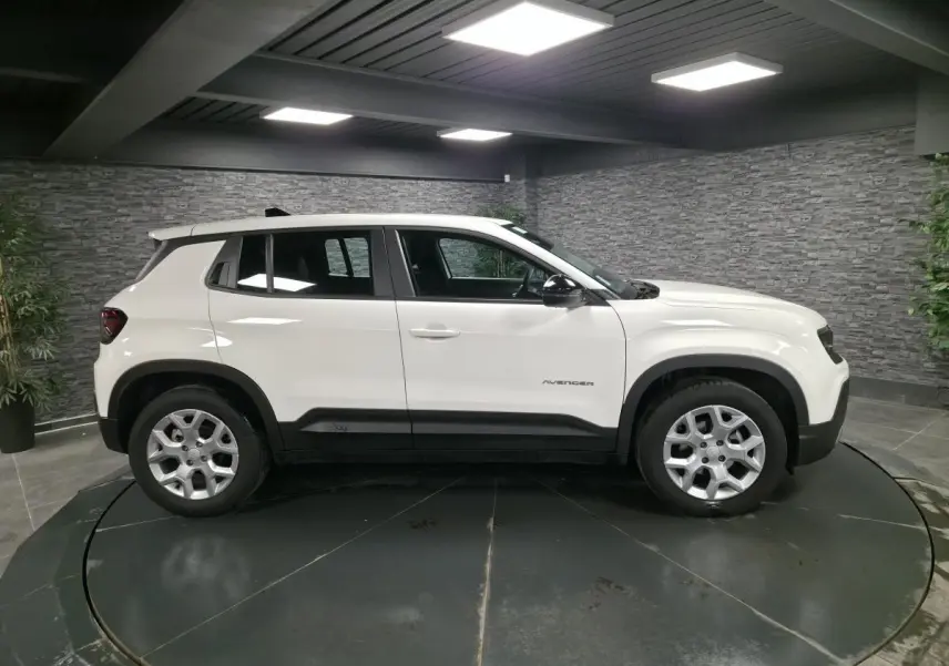 Vue de profil côté gauche d'un Jeep Avenger blanc avec jantes alliage 17 pouces dans un showroom intérieur.