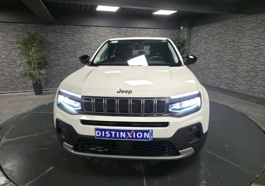 Vue de face du Jeep Avenger blanc avec phares LED allumés et calandre noire distinctive en showroom.