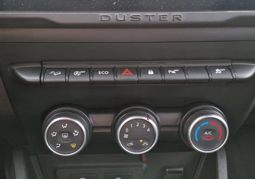 Gros plan sur la console centrale du Dacia Duster blanc 2023, montrant les commandes de climatisation et les boutons de fonction.