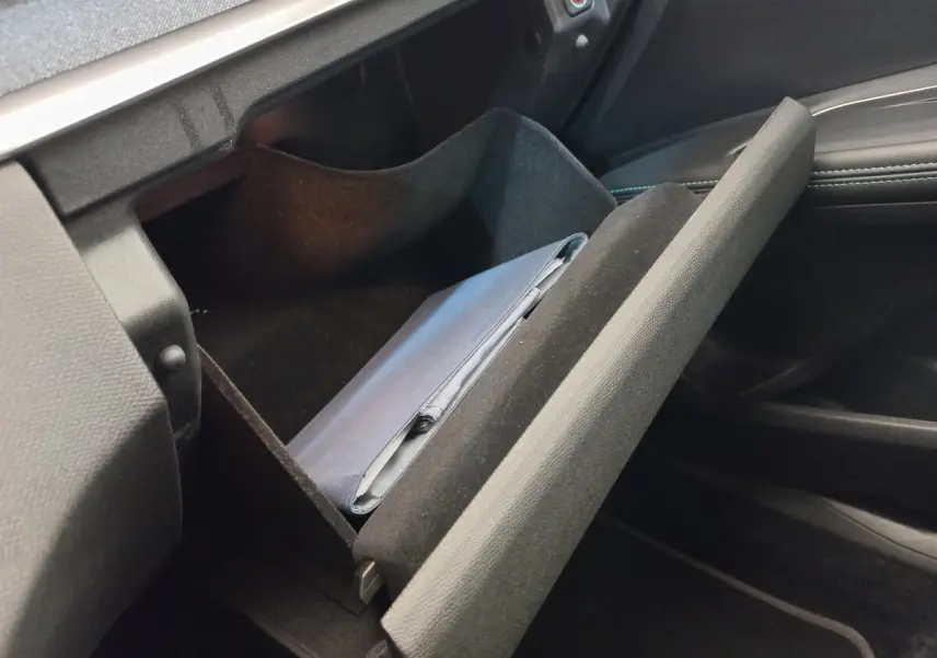 Gros plan sur la boîte à gants ouverte du Peugeot 5008 gris foncé, montrant un carnet de bord à l'intérieur.