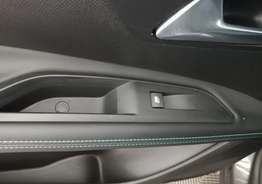 Gros plan sur la commande de lève-vitre côté gauche du Peugeot 5008 gris foncé avec surpiqûres bleues sur la porte.