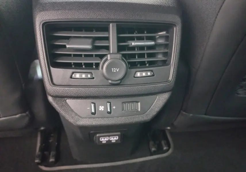 Gros plan sur la console arrière noire du Peugeot 5008 2021 avec prise 12V, commandes ventilation et ports USB visibles.
