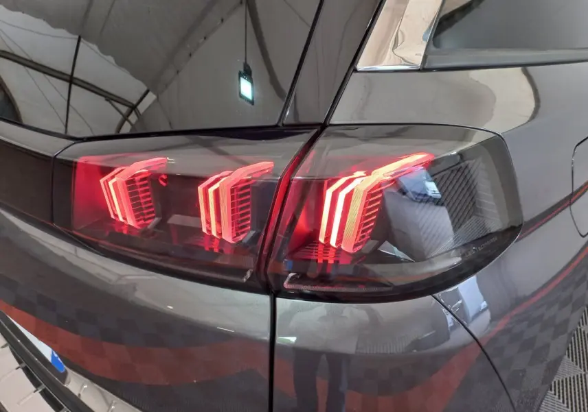 Gros plan sur les feux arrière allumés côté gauche d'un Peugeot 5008 gris foncé dans un garage.