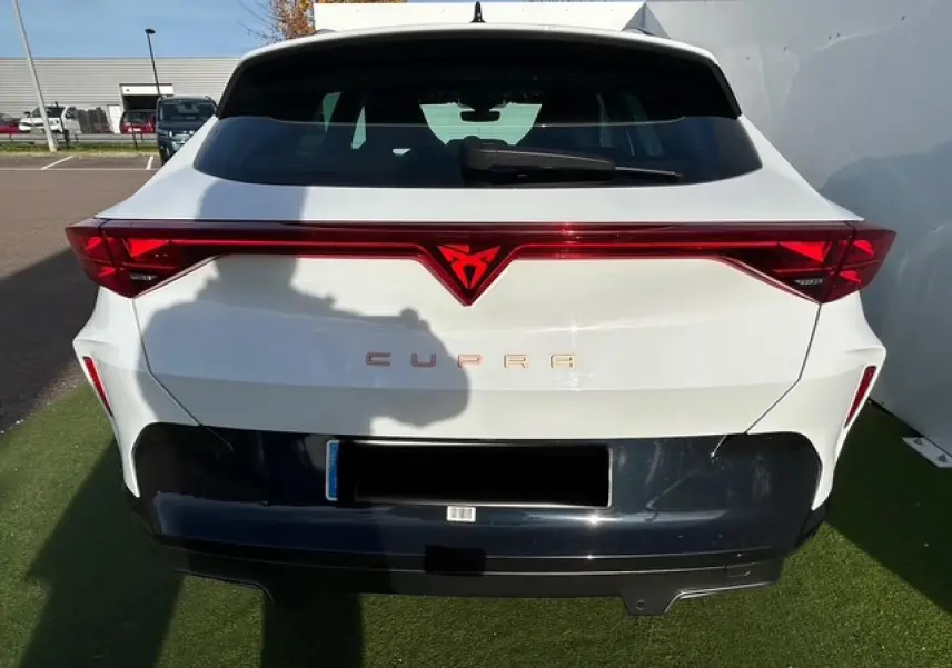 Vue arrière d'une CUPRA Formentor blanc neige avec bandeau lumineux rouge et logo CUPRA éclairé au centre.