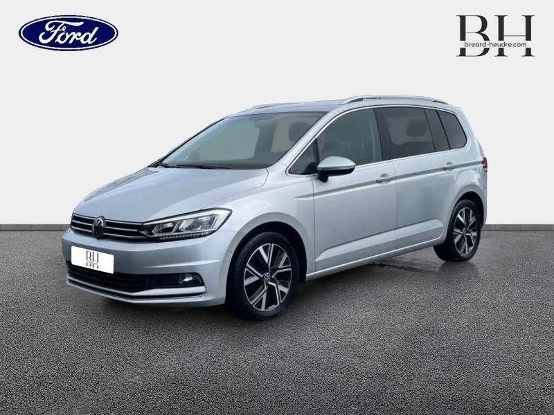 Volkswagen Touran 1.5 TSI Carat 7 places en Reflet d'Argent, vue 3/4 avant avec jantes alliage et barres de toit.