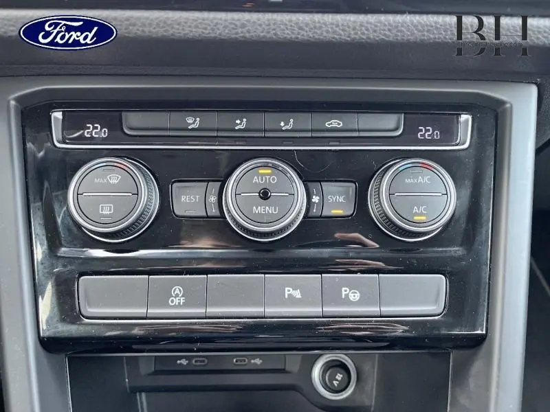 Gros plan sur la console centrale noire du Volkswagen Touran 1.5 TSI, montrant les commandes de climatisation et boutons multifonctions.