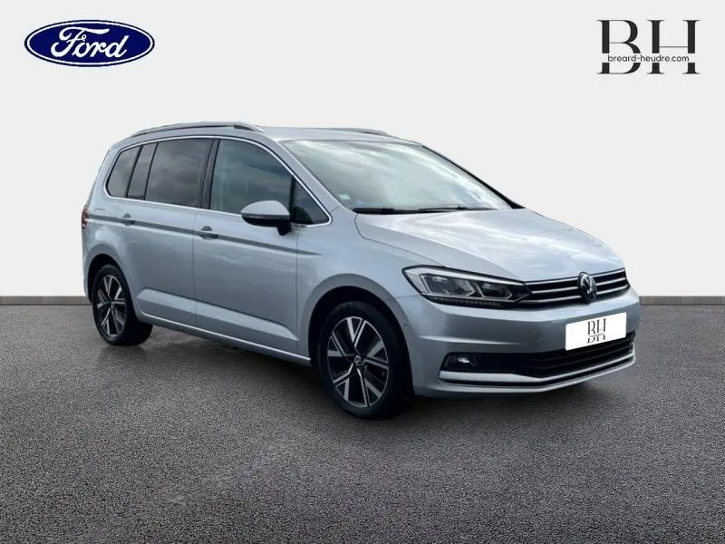 Volkswagen Touran 1.5 TSI Carat 7 places en reflet d'argent métallisé, vue 3/4 avant droit avec jantes alu noires.