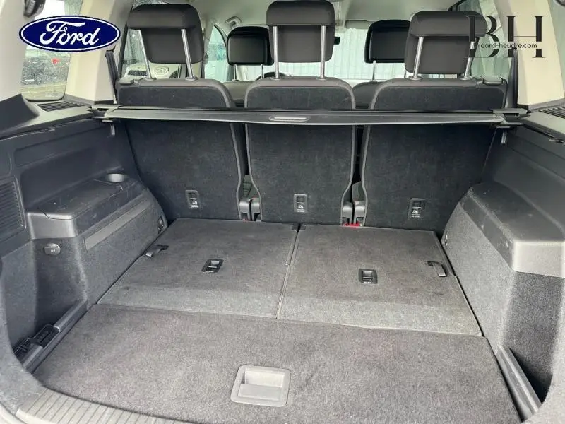 Coffre ouvert vu de l'arrière d'un Volkswagen Touran 1.5 TSI argent métallisé avec sièges arrière rabattus et cache-bagages.