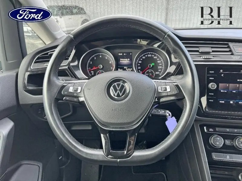 Vue intérieure centrée sur le volant cuir noir du Volkswagen Touran 2021 avec tableau de bord et écran tactile visibles.