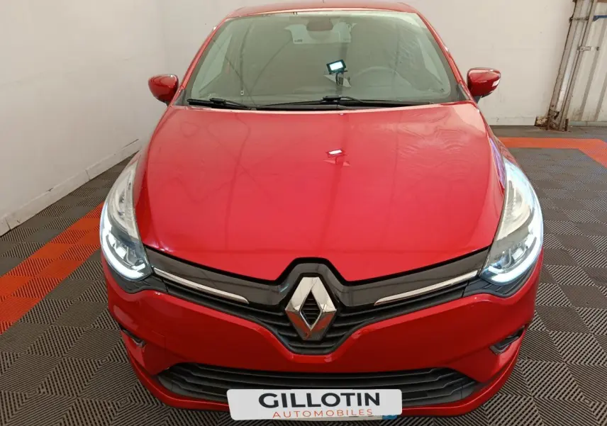 Vue frontale rapprochée d'une Renault Clio Intens rouge avec phares LED allumés dans un garage.