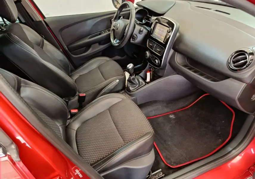 Vue intérieure côté conducteur de la Renault Clio Intens rouge, montrant sièges noirs et tableau de bord avec écran tactile.