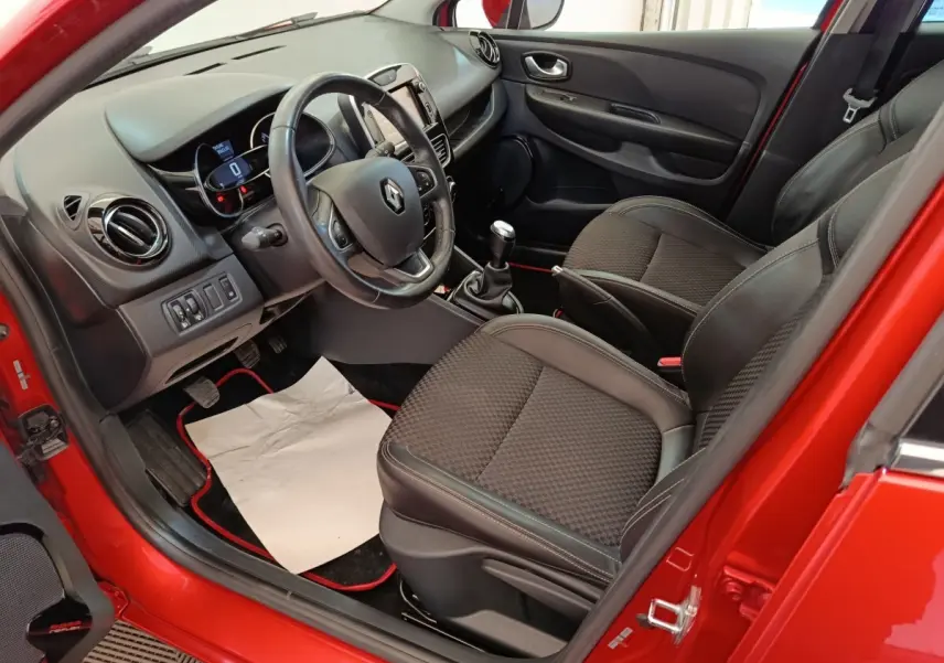 Vue intérieure côté conducteur de la Renault Clio rouge 2018, avec volant cuir et boîte manuelle visible.