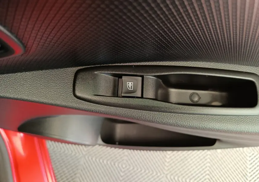 Gros plan sur la commande de lève-vitre côté conducteur d’une Renault Clio Intens rouge, intérieur noir texturé.