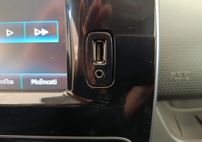 Gros plan sur la prise USB et prise jack intégrées à la console centrale noire d'une Renault Clio Intens rouge.