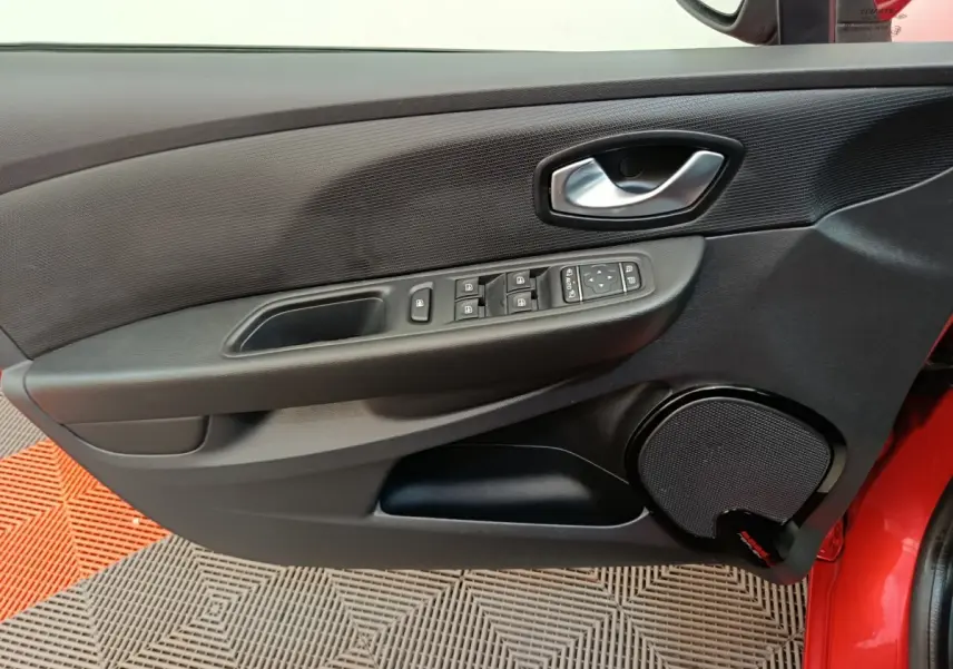 Vue rapprochée de la porte avant gauche rouge de la Renault Clio Intens avec commandes de vitres et haut-parleur intégré.