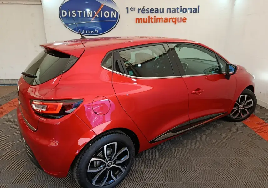 Renault Clio Intens rouge vue 3/4 arrière droit, avec jantes alliage et toit spoiler en intérieur showroom.