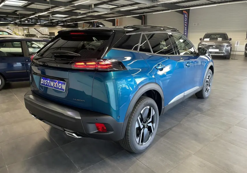 Peugeot 2008 hybride bleu vue 3/4 arrière droit en intérieur avec toit noir et feux arrière LED allumés.