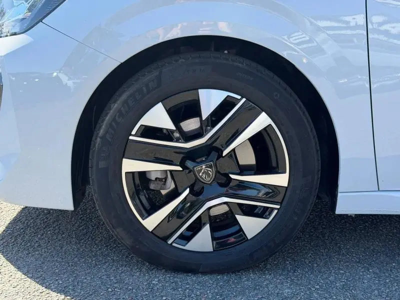 Gros plan sur la roue avant droite d'une Peugeot 208 blanche avec jante alliage noire et argentée.