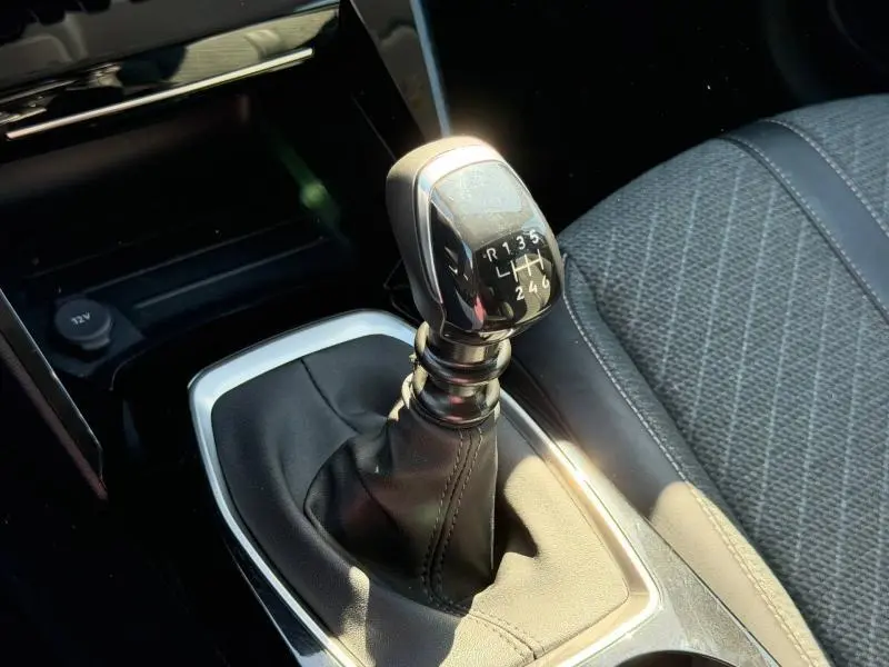 Gros plan sur le levier de vitesses manuel noir de la Peugeot 208, avec sellerie tissu gris à motifs visibles à droite.