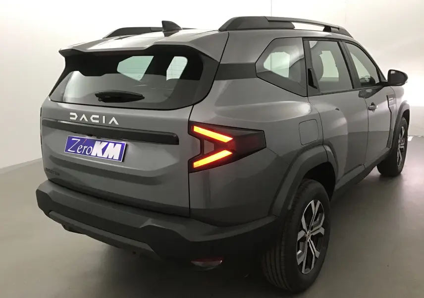 Vue 3/4 arrière droite du Dacia Bigster gris schiste avec feux arrière allumés et logo DACIA visible sur le hayon.