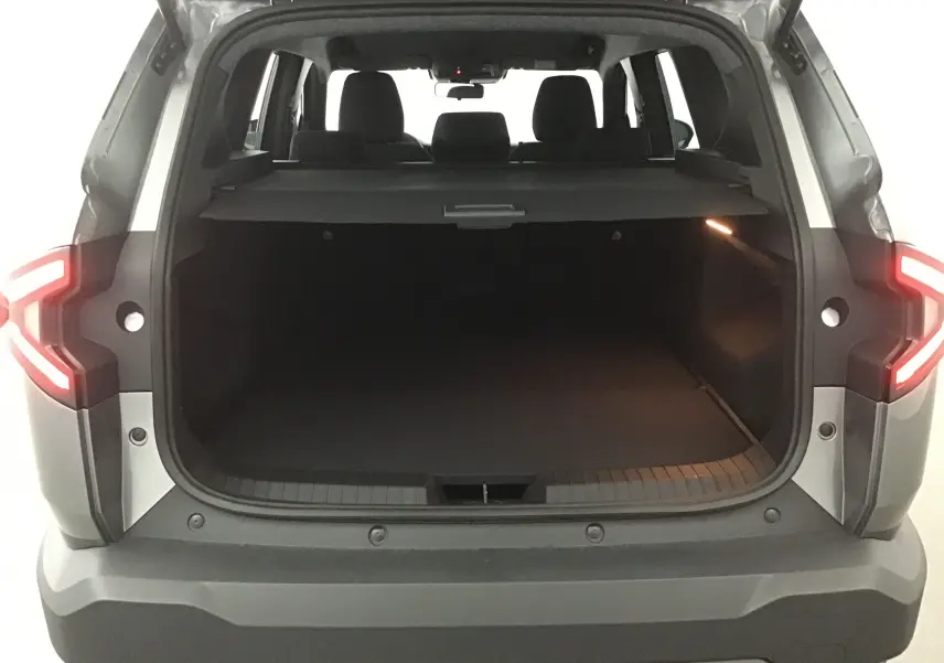 Vue arrière du coffre ouvert du Dacia Bigster gris schiste 2025, avec feux arrière allumés et banquette visible.