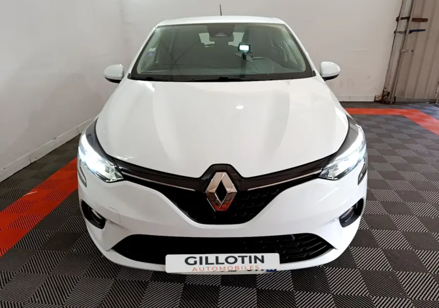 Vue frontale d'une Renault Clio Business blanche avec phares LED allumés sur sol damier noir et rouge.