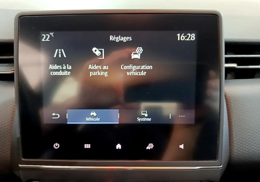 Écran tactile central du tableau de bord de la Renault Clio Business blanc, affichant les réglages d'aides à la conduite et parking.