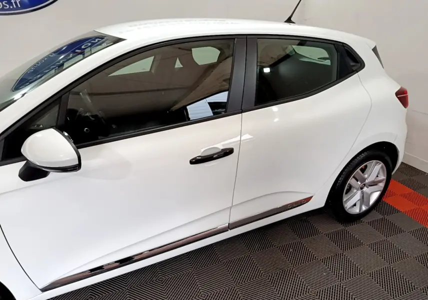 Profil côté gauche d'une Renault Clio Business blanche, avec poignées noires et jantes alliage visibles sur fond intérieur.