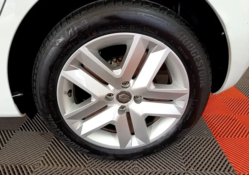 Gros plan sur la roue arrière droite d'une Renault Clio Business blanche, avec pneu Bridgestone visible sur sol carrelé noir et rouge.