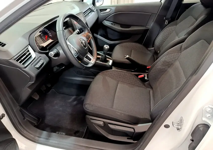 Vue intérieure côté conducteur de la Renault Clio Business blanche, montrant sièges tissu noir et volant cuir multifonctions.