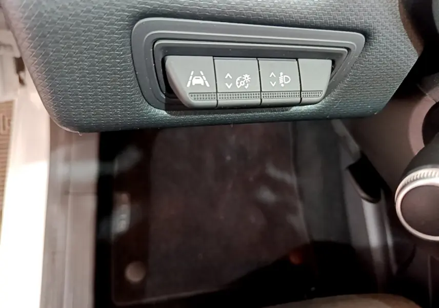 Gros plan sur les commandes d'assistance à la conduite sous le tableau de bord d'une Renault Clio Business blanche.