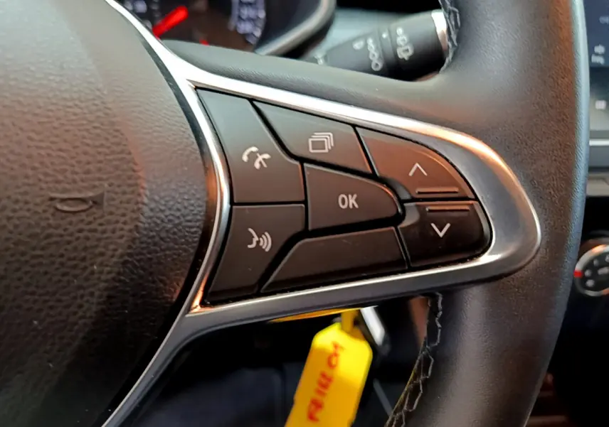 Gros plan sur les commandes multifonctions du volant cuir noir de la Renault Clio Business blanche de 2021.