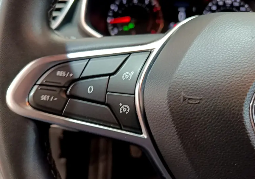 Gros plan sur les commandes du volant côté gauche de la Renault Clio Business blanche, avec tableau de bord flou en arrière-plan.