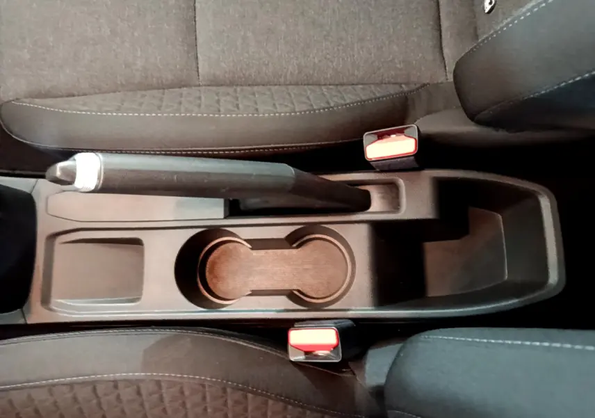 Vue plongeante sur la console centrale noire de la Renault Clio Business avec frein à main manuel et porte-gobelets.