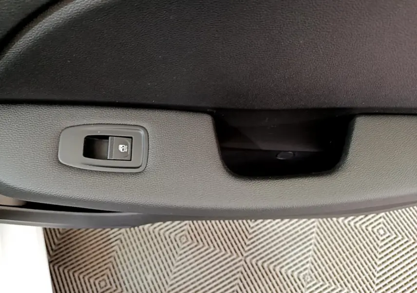 Gros plan sur la commande de verrouillage de porte noire dans l'habitacle d'une Renault Clio Business blanche, côté conducteur.