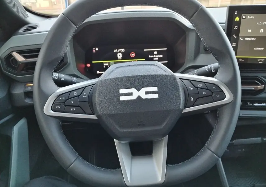 Vue rapprochée du volant noir du Dacia Bigster 2025 avec commandes intégrées et tableau de bord numérique allumé.