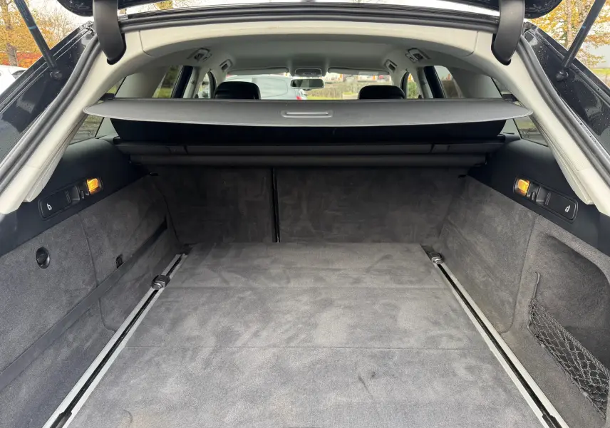 Coffre spacieux et propre de l’Audi A6 Avant noir, vue depuis l’arrière avec la trappe ouverte et cache-bagages déployé.