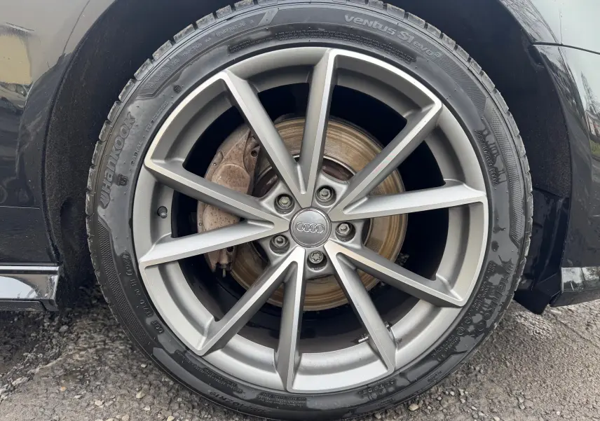 Gros plan sur la roue avant droite d’une Audi A6 Avant noire de 2015 avec jante alliage 19 pouces à dix branches.