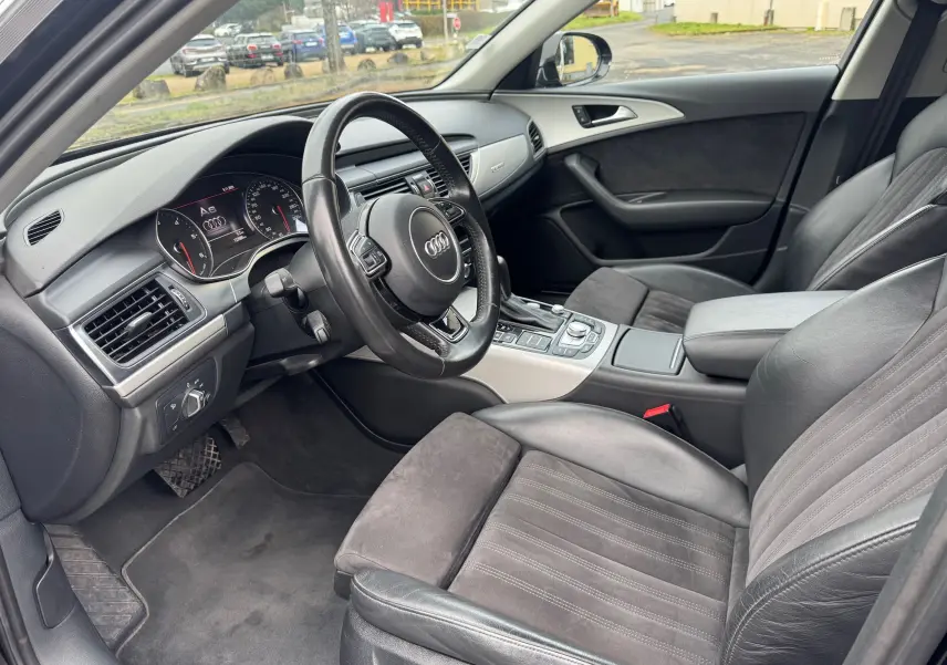 Vue intérieure côté conducteur de l’Audi A6 Avant 2015, sièges cuir noir et tableau de bord moderne avec volant multifonction.