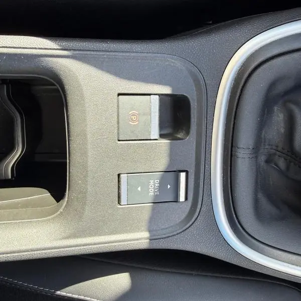 Vue rapprochée de la console centrale noire du Jeep Avenger 2025, montrant le frein à main électrique et le bouton Drive Mode.